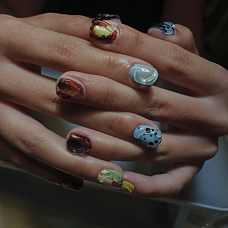 Manos entrelazadas con uñas en carey, cromo plateado en relieve y azul con puntos negros.