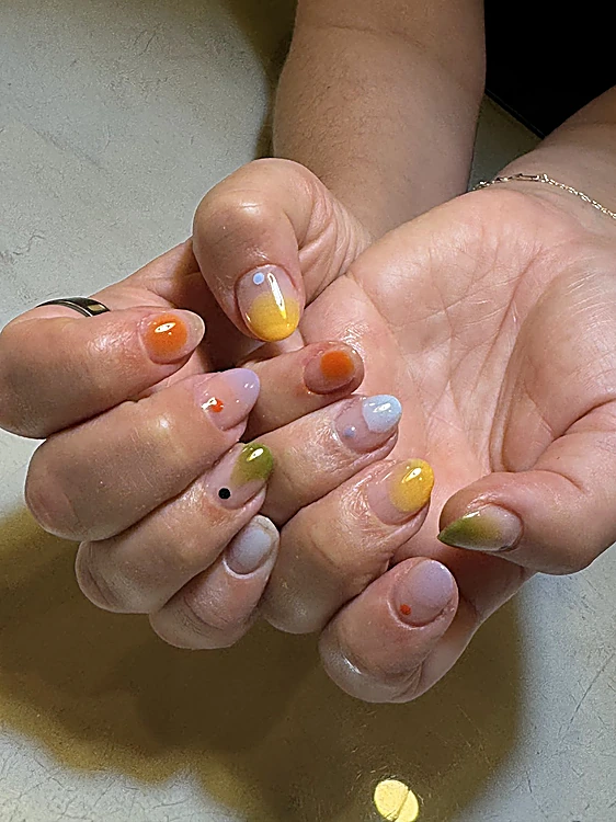 Palmas abiertas con uñas cortas, cada una con un degradado o punto de color distinto: amarillo, naranja, verde y lila.