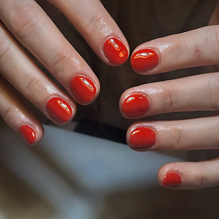 Dos manos abiertas con uñas cortas en rojo liso y brillante.