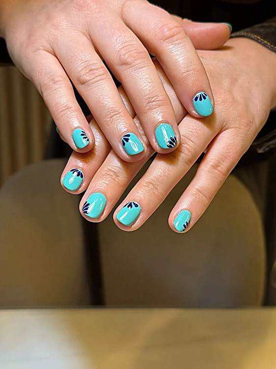 Manos cruzadas con uñas cortas turquesa y una flor azul marino pintada a mano en la base.